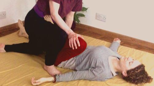 Thai massage in progress: a clothed client lying on a futon mat receiving a leg stretch